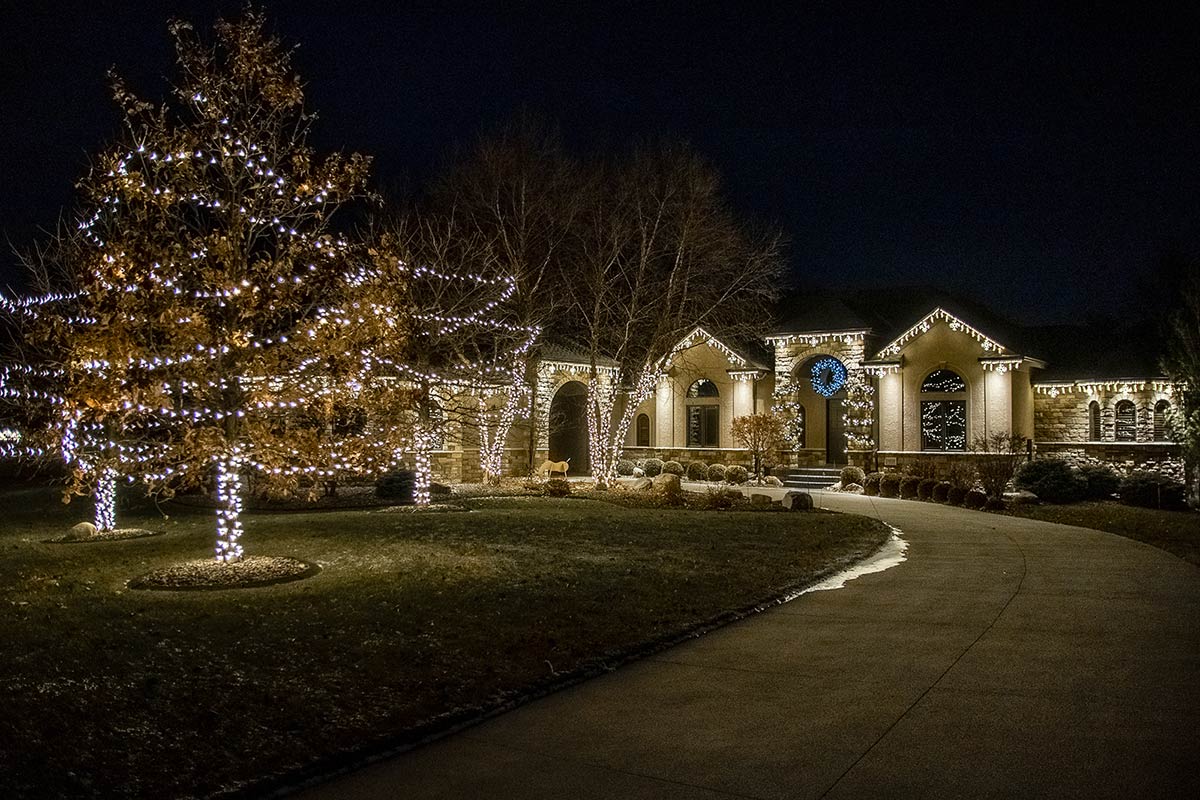 trees and home decorated with white lights and blue wreath